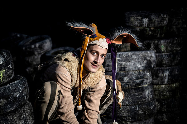 Ein verkleideter Schauspieler hockt auf einer Bühne.