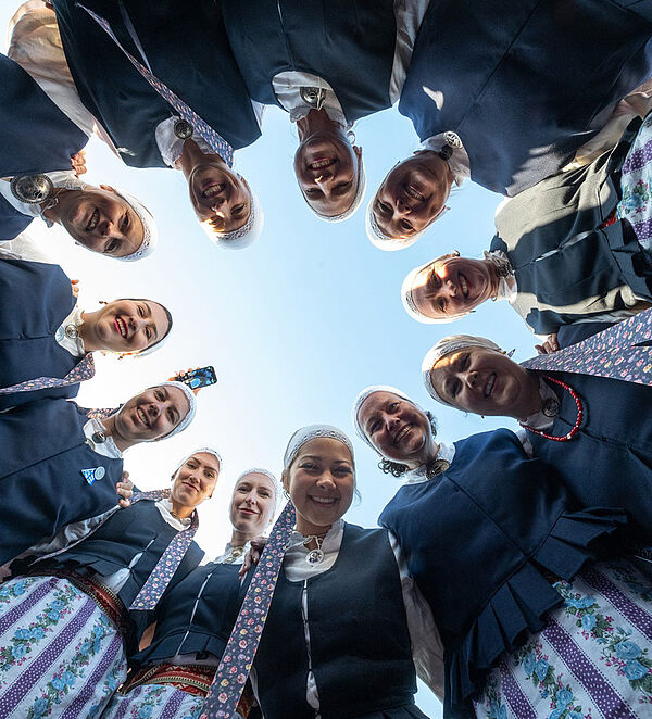 12 Frauen stehen in einem Kreis. Sie schauen von oben in die Kamera. Sie tragen estnische Trachten. 