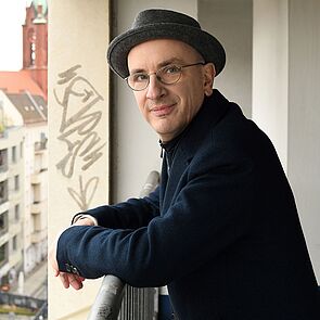 Der Autor Hein Jakob steht auf einem Balkon.