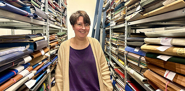 Eine Frau steht zwischen zwei Regalen. In den Regalen liegen viele Mappen.