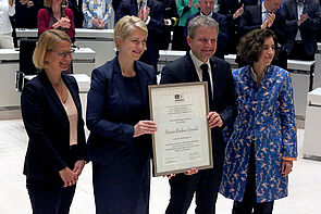 Drei Frauen und ein Mann präsentieren eine Urkunde.