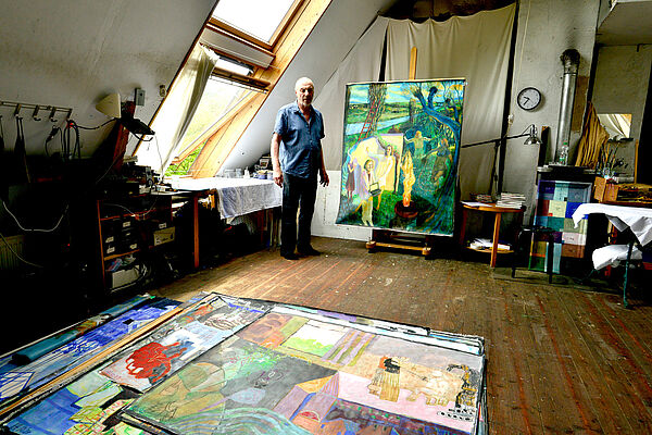 Heinke Holm in seinem Atelier. Er steht neben einem großformatigen Bild. Auf dem Boden liegen weitere Bilder.