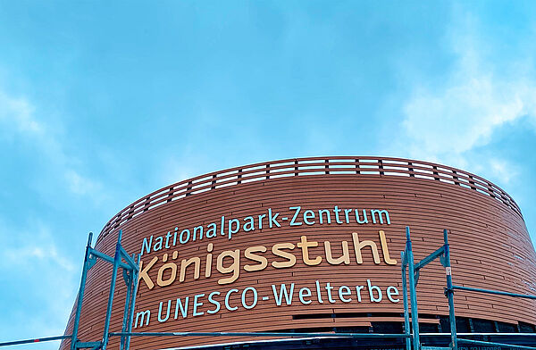 Der Eingangsbereich von außen. An der Fassade des Rundbaus steht „Nationalpark-Zentrum Königsstuhl im Unesco-Welterbe.