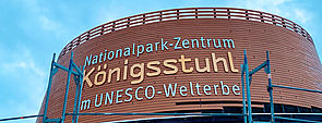 Der Eingangsbereich von außen. An der Fassade des Rundbaus steht „Nationalpark-Zentrum Königsstuhl im Unesco-Welterbe.