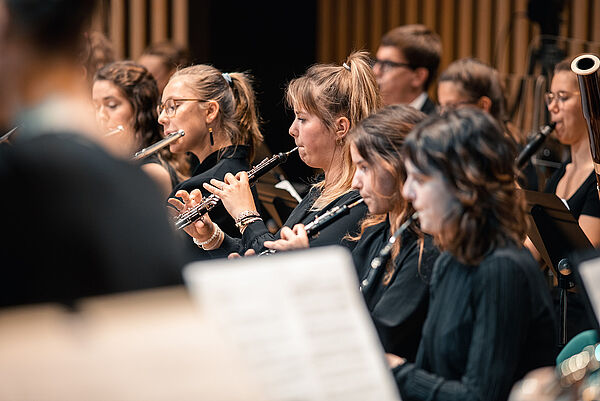 Musiker und Musikerinnen spielen Holzblasinstrumente in einem Orchester.