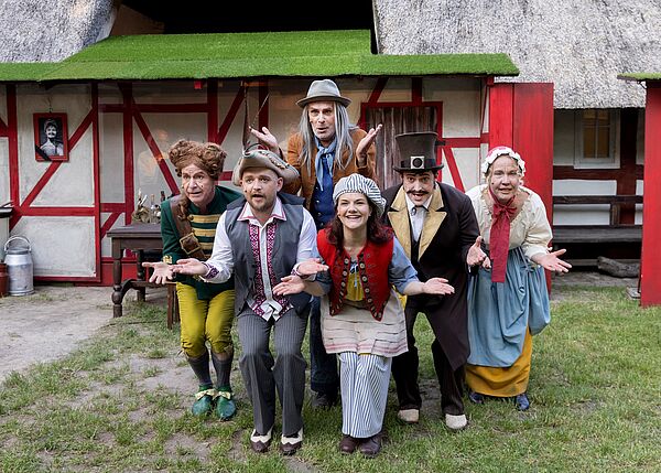Sechs verkleidete Schauspieler schauen gestikulierend in die Kamera.