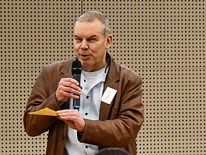 Bernd Lukasch hält einen gelben Zettel und ein Mikrofon in seinen Händen.