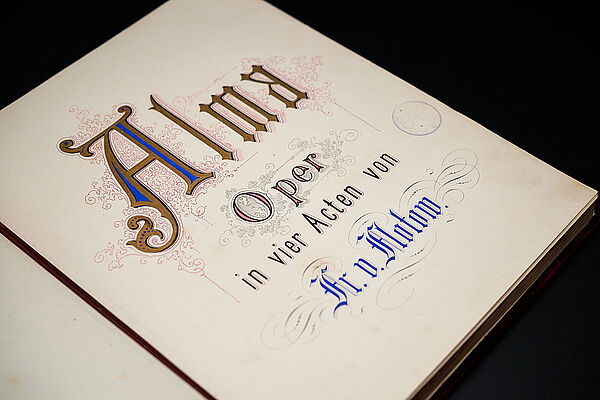 Eine aufgeschlagene Buchseite. Darauf steht: Alma. Oper in vier Akten. Fr. v. Flotow.