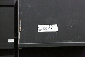 Gasse R2. Ein Hinweis klebt an einer schwarzen Rückeite.