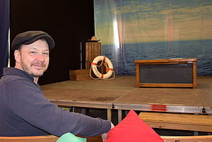 Jens Hasselmann sitzt vor seiner Bühne. Auf der Bühne stehen eine Kiste und ein Rettungsring.