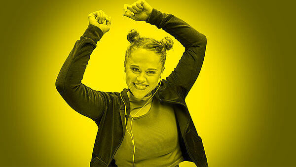 Eine junge Frau tanzt ausgelassen.Das Foto ist knallig gelb.