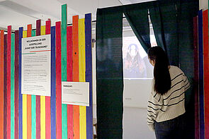 Eine junge Frau hält einen Vorhang auf.