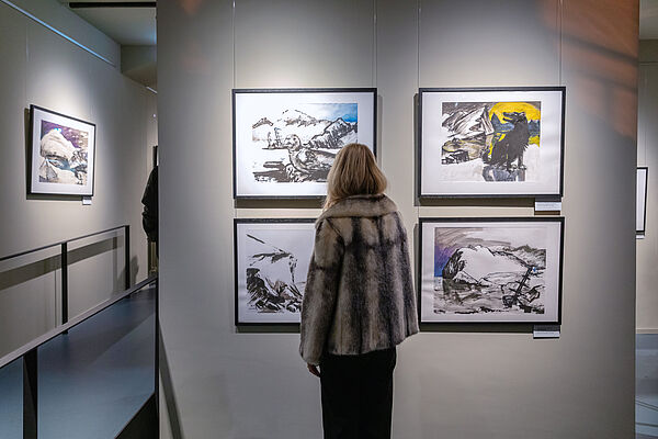 Eine Frau steht vor einer Wand mit mehreren Zeichnungen.