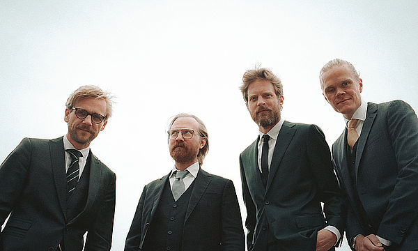 Vier Männer im Anzug vom Danish String Quartet gucken von oben herab. Blauer Hintergrund.
