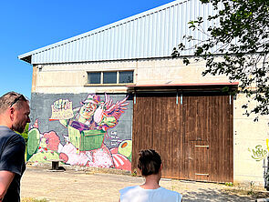 Tino Bittner und Lydia Klammer betrachten eine Industriehalle mit Graffitti.