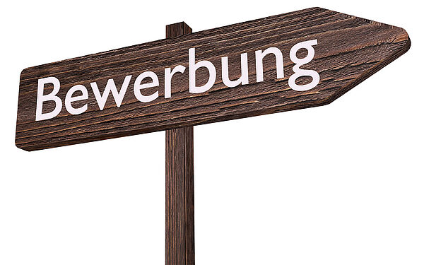 Ein Holzwegweiser, auf dem in weißen Buchstaben "Bewerbung" steht.