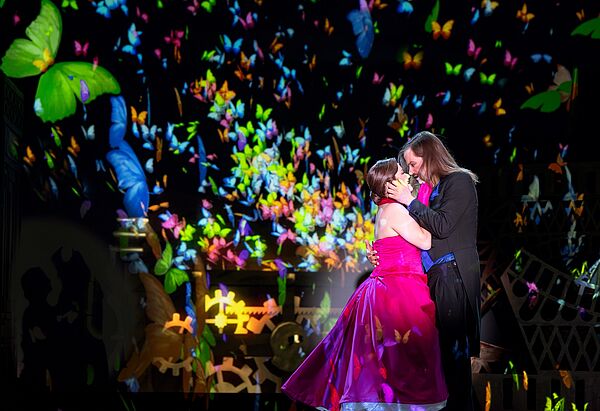 Eine Frau und ein Mann umarmen sich auf einer bunt beleuchteten Bühne.