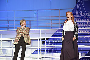 Eine Frau steht auf der Bühne uns singt. Ein Mann lehnt am Deck-Geländer und schaut sie an.