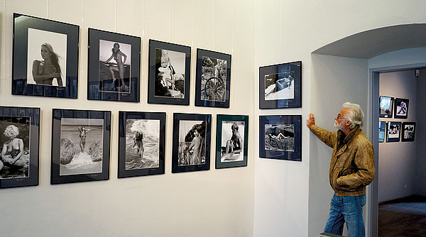 Klaus Ender steht vor einer Wand mit gerahmten Aktfotos.