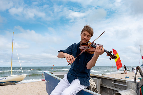 Nils Mönkemeyer lehnt am Strand der Ostsee an einem Boot und spielt auf seiner Bratsche.