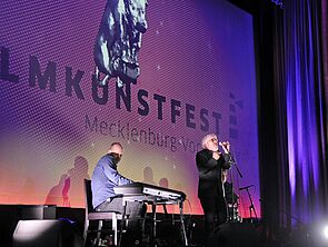 Jes Holtsø steht auf der Bühne uns singt. Ein andere spielt Keyboard. 