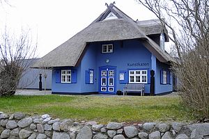 Ein blaues, restgedecktes Haus mit weißen Fenstern, umgeben von Wiese.