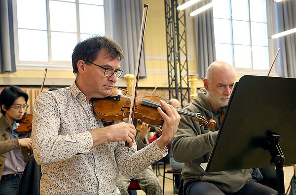 Volker Reinhold spielt eine Geige. Hinter ihm andere Musiker mit Instrumenten.