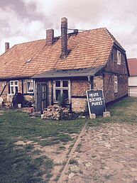 Ein altes Fachwerkhaus, davor eine Wiese und ein gepflasterter Weg. Am Haus lehnt eine kleine Tafel mit der Aufschrift "Heute Büchermarkt".