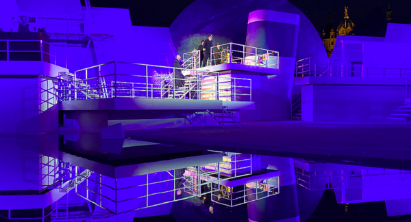 Das Bühnenbild der Titanic ist in blaues Licht getaucht und spiegelt sich im Boden. Die Kommandobrücke ist erleuchtet. Darauf stehen Schauspieler.