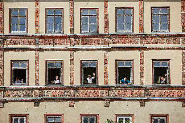 Drei Fensterreihen der Schlossfassade mit jeweils fünf Fenstern nebeneinander. Die Fenster der mittleren Reihe sind geöffnet. Aus jedem Fenster winken Personen.