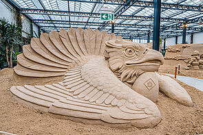 Ein Vogel. Der Vogel ist größer als ein Mensch. Der Vogel ist aus Sand.