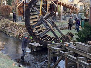 Arbeiter schieben das Wasserrad von seiner Halterung.