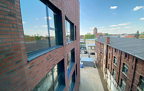 Ein Ziegelsteingebäude schiebt sich von links ins Bild. Im Hintergrund erheben sich die Dächer der Altstadt und eine Kirche.