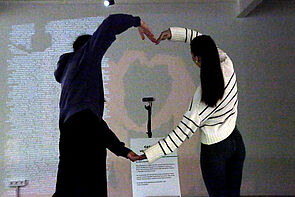 Zwei junge Frauen bilden mit ihren Armen ein Herz nach.