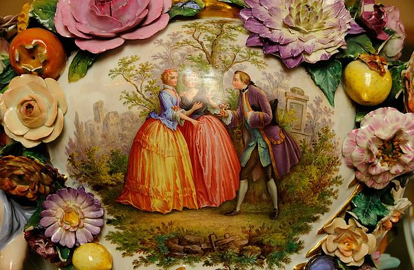 Detailaufnahme von bunten Blüten und einem Bild, auf dem ein Mann vor zwei Frauen steht.