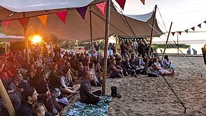 Menschen sitzt an einem Strand unter Zeltplanen im Sonnenuntergang.