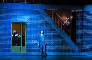 Ein Mann steht an der Wand. Die Bühne ist blau beleuchtet.