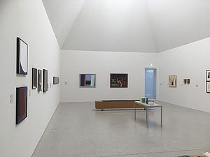 Ein weißer Ausstellungsraum mit Gemälden.