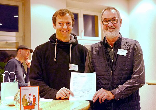 Tom Reimer und Ulf Borkenhagen stehen gemeinsam an einem Tisch und halten das Blatt mit der Absichtserklärung in der Hand.