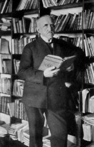 Ein Mann im Anzug steht vor einer Bücherwand. 