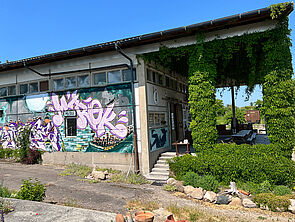 Eine Hallenwand mit Graffitti. Rechts eine Terrasse.