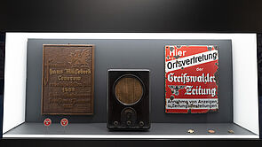 Eine Vitrine mit zwei Schildern und einem Radio aus der Vorkriegszeit des 2. Weltkrieges.