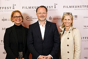 Gruppenbild. Zwei Frauen, in der Mitte steht ein Mann.