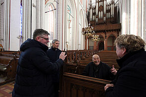Vier Männer in der Kirche. Einer sitzt auf einer Bank.