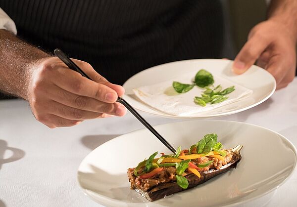 Ein Koch drapiert mit einer Pinzette Essen auf einem Teller.