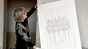 Eine Frau hält eine Zeichnung der Skulpturen in den Händen. 