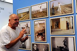 Holger Stark steht vor einer Wand mit seinen Bildern. 