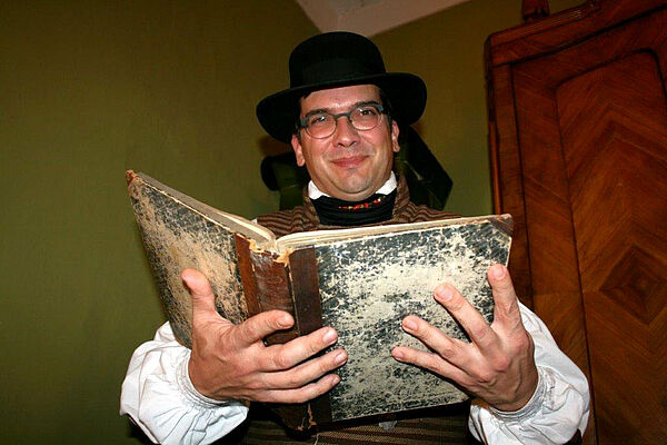 Olaf Both trägt eine historische Tracht und hält ein aufgeschlagenes historisches Buch in seinen Händen. 