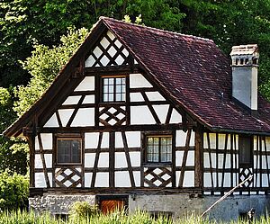 Ein weißes Haus. In den Wänden sind schwarze Linien. Die schwarzen Linien sind Holzbalken.