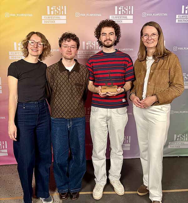 Ein Gruppenfoto. Links und rechts stehen zwei Frauen, in der Mitte zwei Männer.